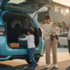 家族が旅行の準備で、トヨタのシエンタのトランクに荷物を積み込んでいる様子。父親がスマートフォンを見ながら、母親は赤ちゃんを抱っこし、幼い息子が自ら荷物を運び入れている。日本の住宅街の夕暮れ時、車は水色。