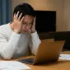 カーリースの審査結果をパソコンで確認し、頭を抱えて悩んでいる日本人男性の様子