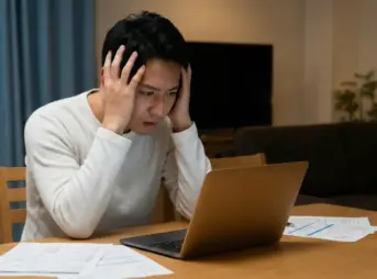 カーリースの審査結果をパソコンで確認し、頭を抱えて悩んでいる日本人男性の様子