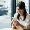 カフェでスマートフォンを見ながら、カーリースの審査について不安そうな表情を浮かべる日本人女性。