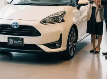 ディーラーでトヨタ シエンタの受注停止と納期未定について説明を受け、困惑する日本人女性客と営業担当者の様子。