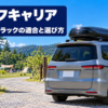 晴れたキャンプ場の入口で屋根にルーフボックスを載せたミニバンの後ろ姿